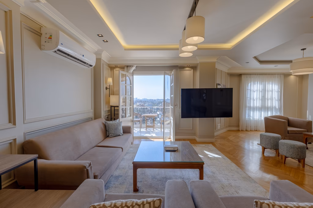 Modernes Wohnzimmer mit beige Möbeln, großem TV, Balkon mit Stadtblick und eleganter Deckenbeleuchtung.